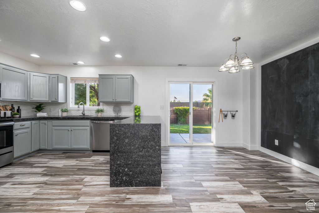 Kitchen with stainless steel appliances, gray cabinetry, wood finished floors, recessed lighting, and a chandelier