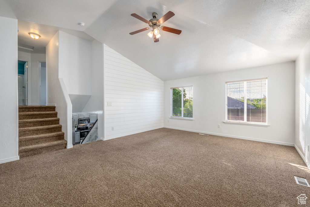 Unfurnished living room with carpet, a ceiling fan, vaulted ceiling, and stairway