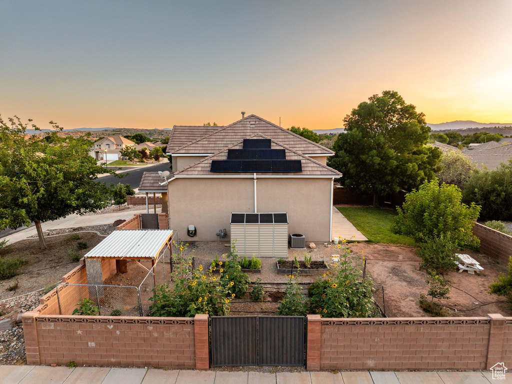 Property exterior at dusk with a gate, roof mounted solar panels, and stucco siding