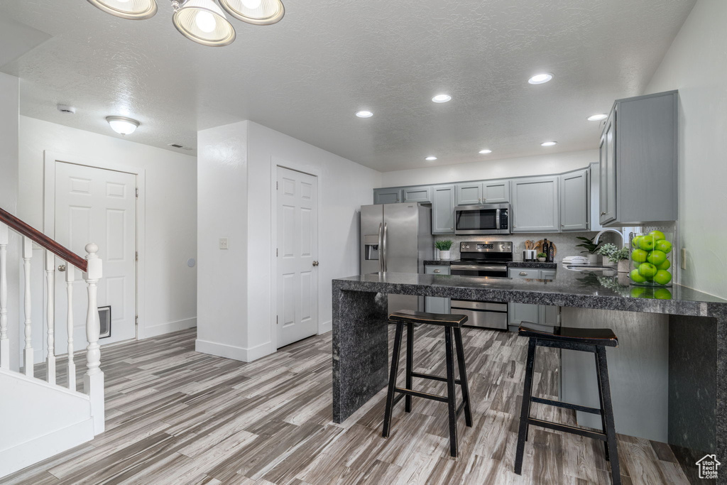 Kitchen with appliances with stainless steel finishes, gray cabinetry, a peninsula, light wood-style floors, and recessed lighting