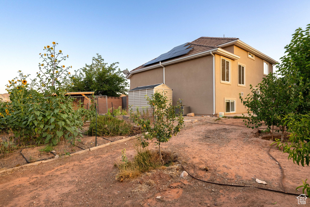 View of side of home featuring a storage unit, solar panels, and stucco siding
