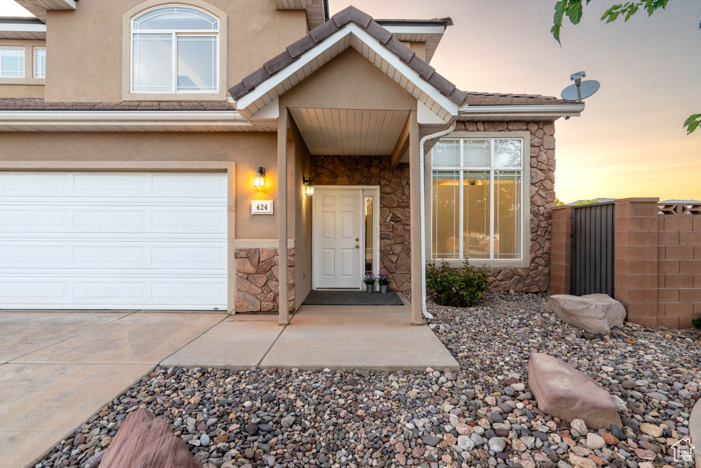 Property entrance with stone siding, driveway, stucco siding, and an attached garage