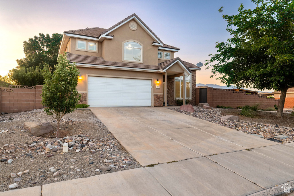 Traditional-style house featuring driveway, an attached garage, stucco siding, a tiled roof, and stone siding