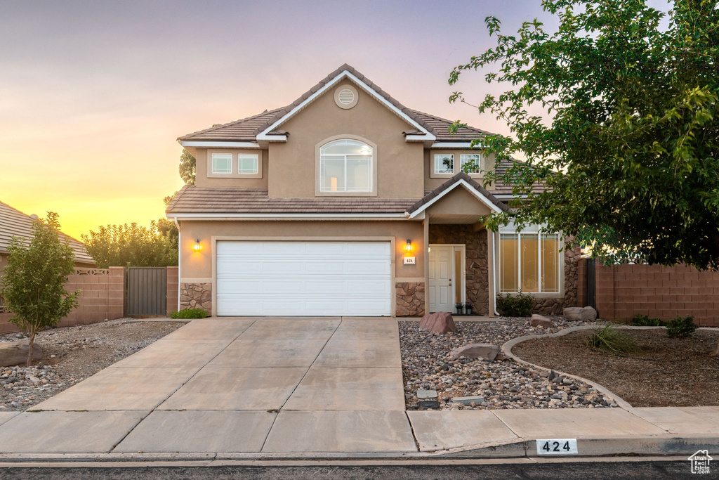 Traditional home featuring stone siding, driveway, an attached garage, stucco siding, and a tiled roof