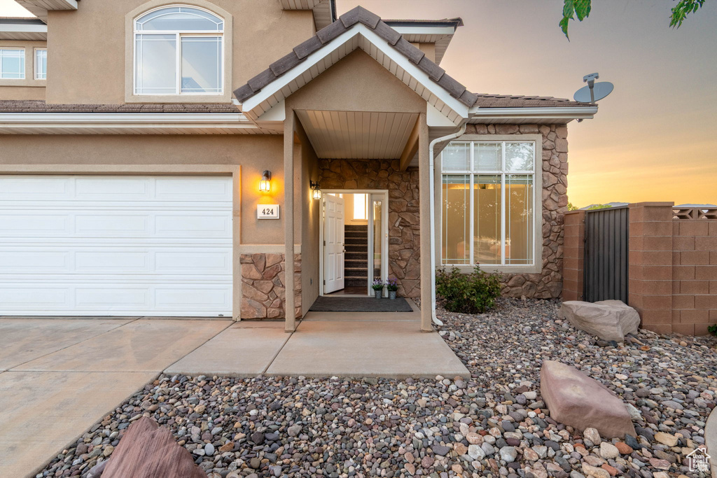 Entrance to property featuring stone siding, driveway, stucco siding, and an attached garage