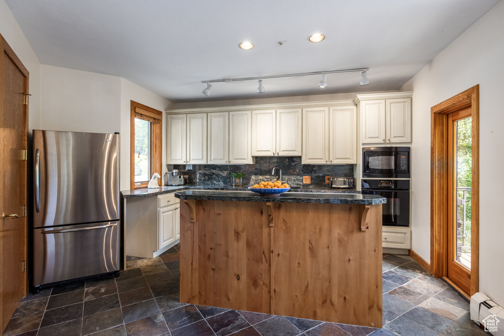 Kitchen with black appliances, a baseboard radiator, stone tile flooring, a center island, and backsplash