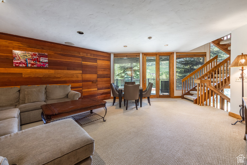 Living area featuring healthy amount of natural light, wooden walls, carpet flooring, and stairs