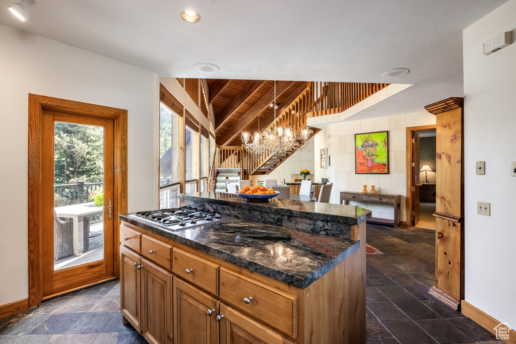 Kitchen with stainless steel gas cooktop, a chandelier, dark countertops, stone tile flooring, and wooden ceiling