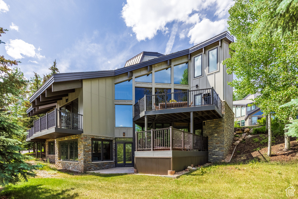Back of property featuring stone siding, a lawn, and a balcony