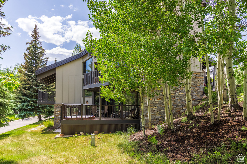 Rear view of house with a balcony, stone siding, a yard, and a wooden deck