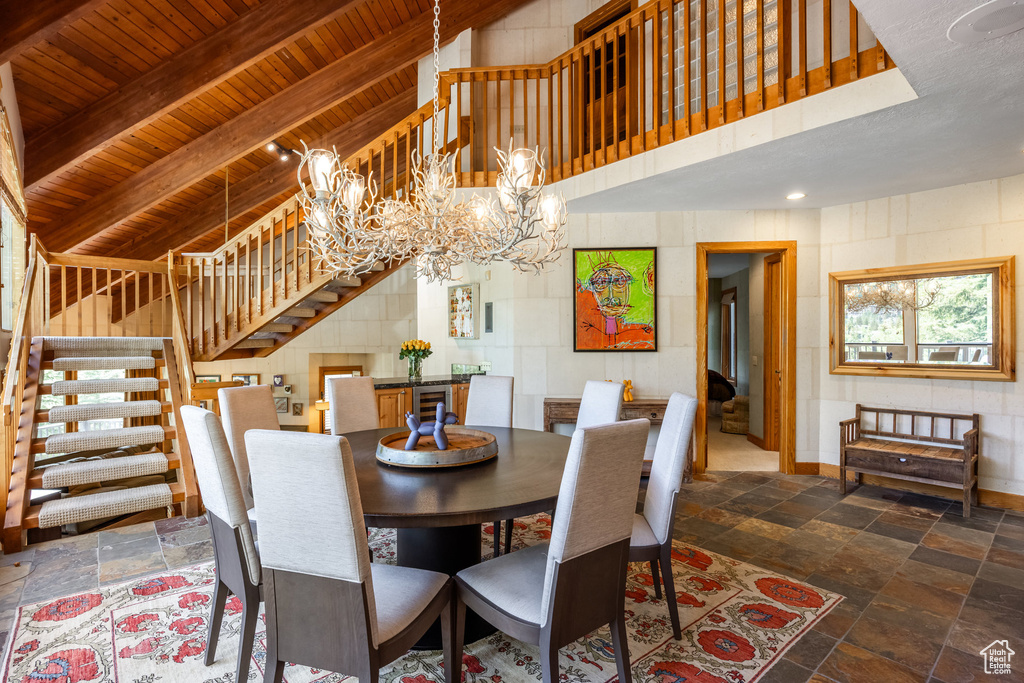 Dining space featuring a wood ceiling with exposed beams, stairway, stone tile floors, a chandelier, and a high ceiling