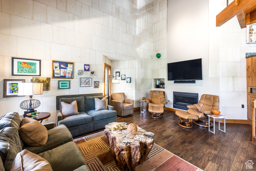 Living area with a glass covered fireplace, wood finished floors, and a towering ceiling