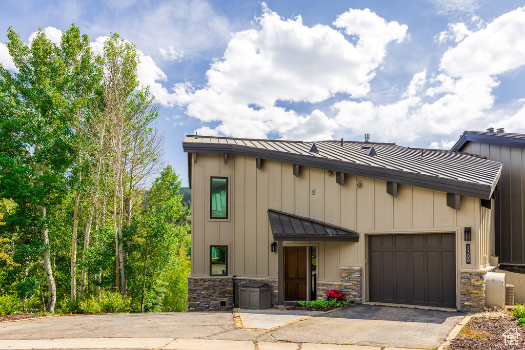 View of front facade featuring a standing seam roof, asphalt driveway, a garage, a metal roof, and stone siding