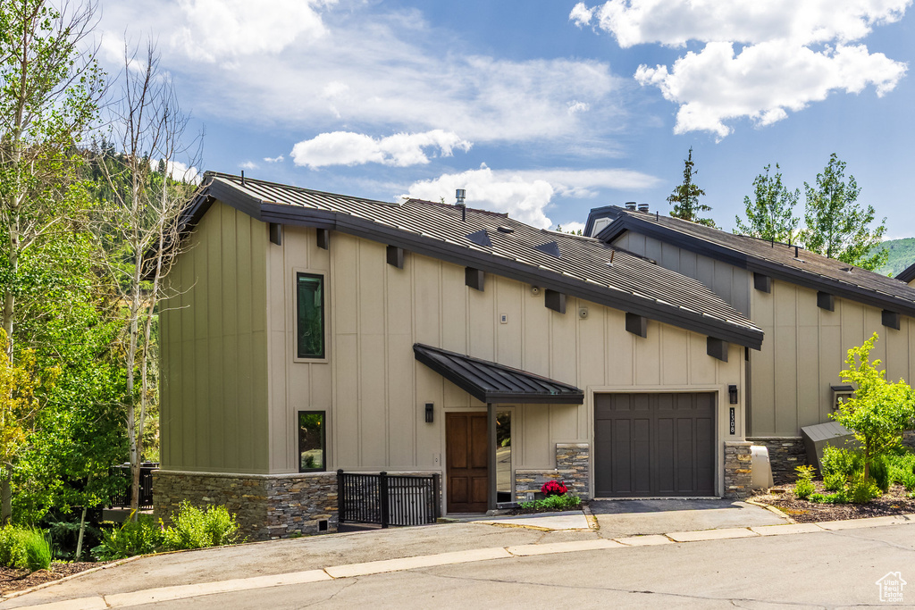 View of front facade featuring stone siding, an attached garage, a metal roof, and driveway