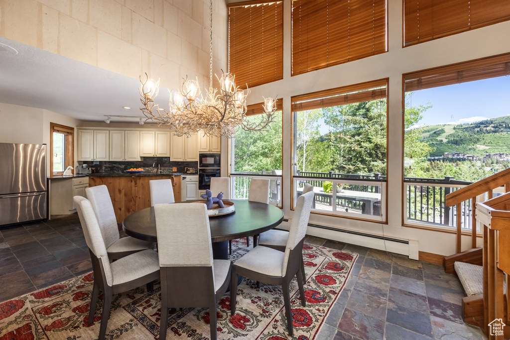 Dining room with stone tile flooring, a chandelier, baseboard heating, and a high ceiling