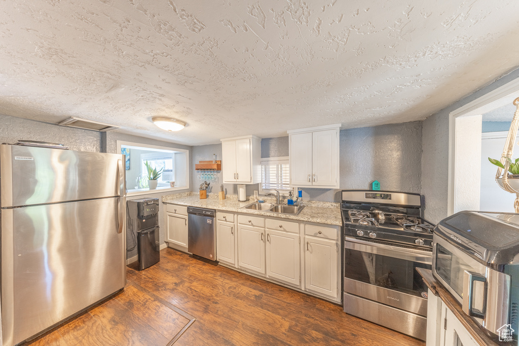 Kitchen with stainless steel appliances, dark wood-type flooring, a textured ceiling, and white cabinetry