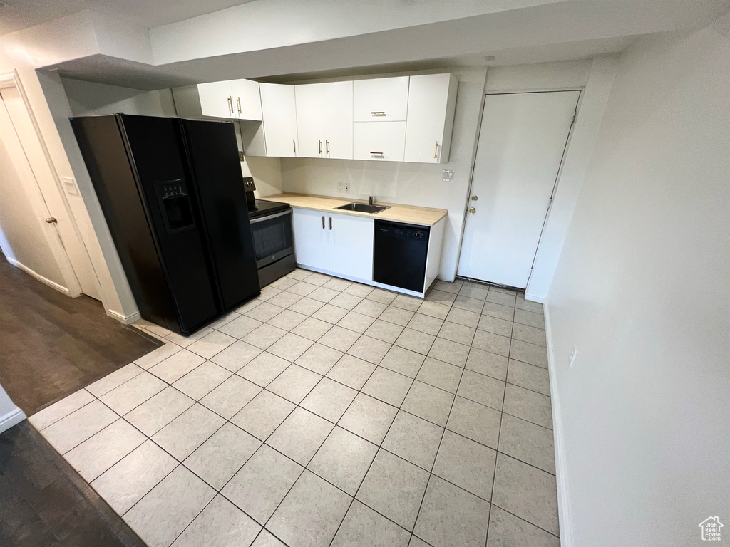 Kitchen featuring black appliances, light tile patterned flooring, light countertops, and white cabinets