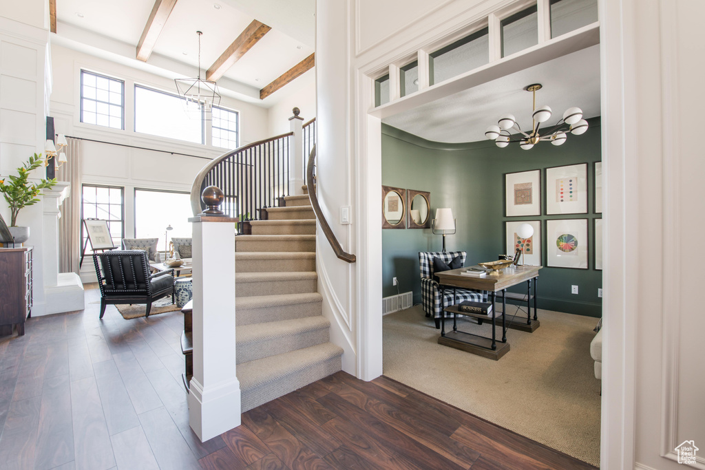 Stairway with a chandelier, wood finished floors, a towering ceiling, and beamed ceiling