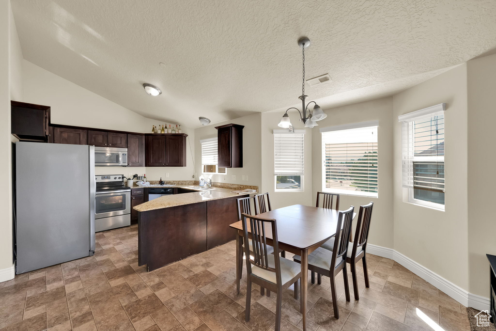 Kitchen featuring stainless steel appliances, dark brown cabinetry, a chandelier, a peninsula, and stone finish flooring