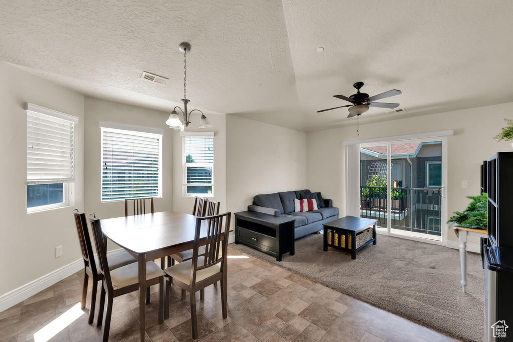 Dining space featuring healthy amount of natural light, ceiling fan, a chandelier, stone finish floors, and a textured ceiling