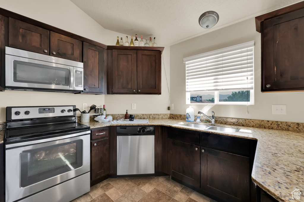 Kitchen with stainless steel appliances, dark brown cabinetry, stone finish flooring, and light stone countertops