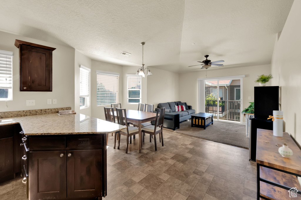 Kitchen with dark brown cabinetry, ceiling fan, open floor plan, hanging light fixtures, and light stone countertops