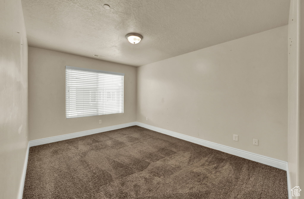 Empty room featuring dark colored carpet and a textured ceiling