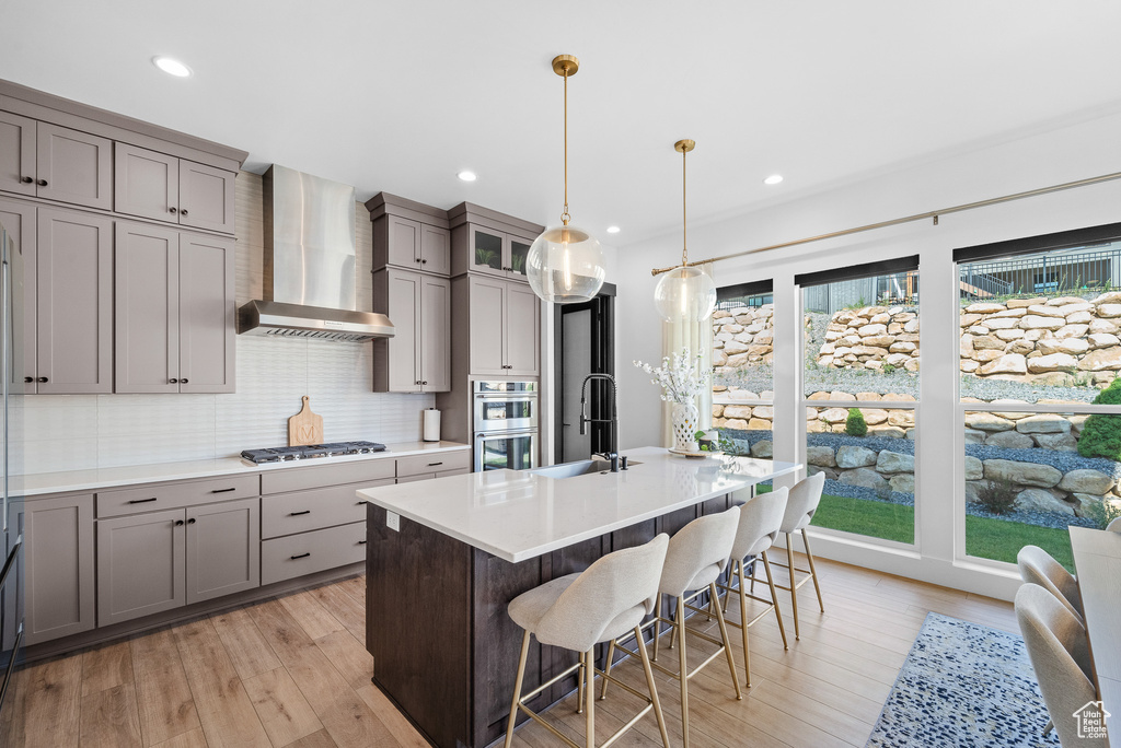 Kitchen featuring wall chimney exhaust hood, gray cabinets, appliances with stainless steel finishes, tasteful backsplash, and recessed lighting