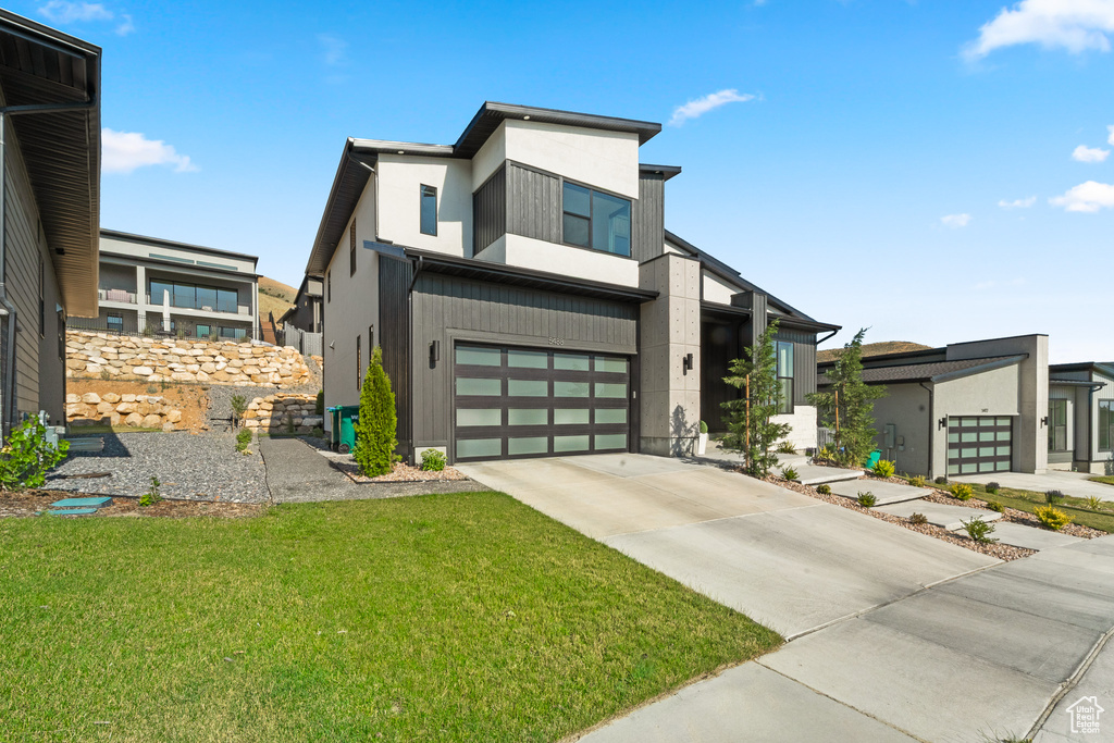 Contemporary house with concrete driveway, an attached garage, and a front yard