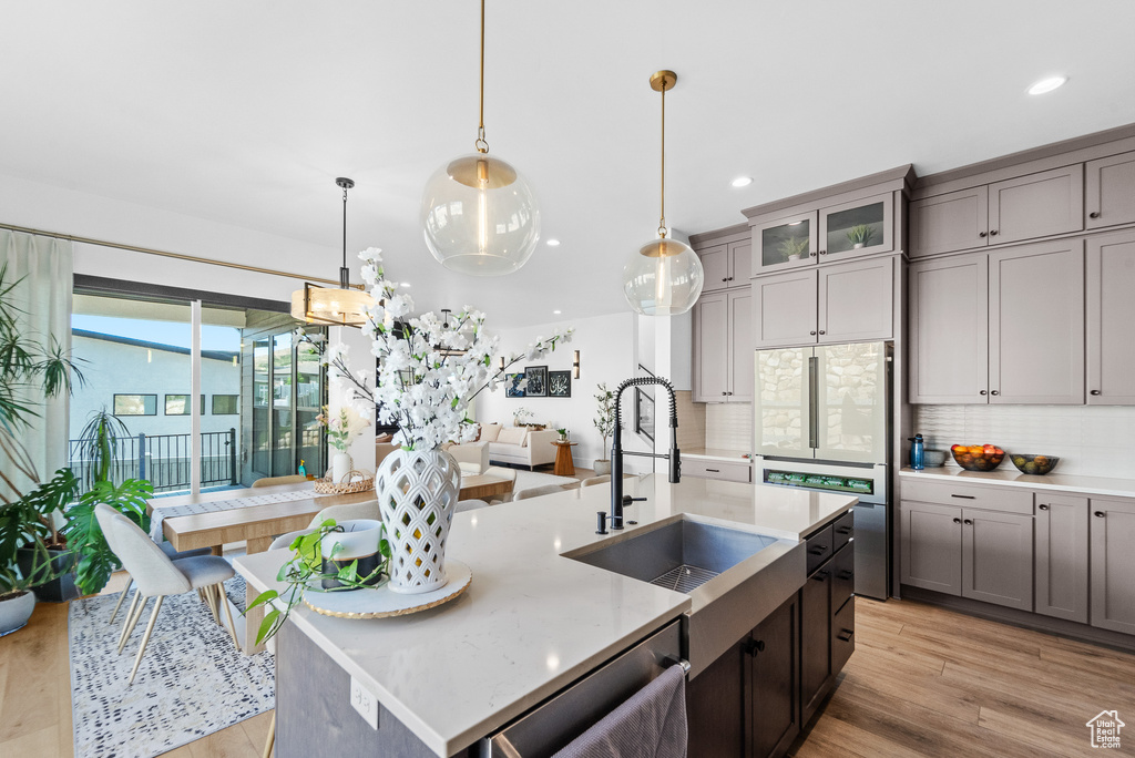 Kitchen featuring backsplash, light wood-type flooring, gray cabinets, a kitchen island with sink, and dishwasher