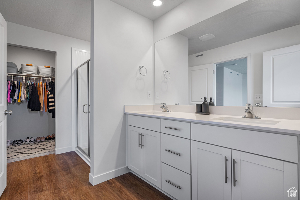 Bathroom with double vanity, wood finished floors, a shower stall, a walk in closet, and recessed lighting