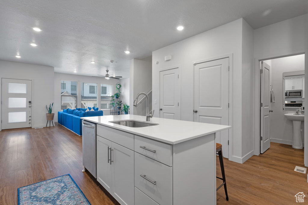 Kitchen with appliances with stainless steel finishes, dark wood-type flooring, white cabinetry, a breakfast bar area, and recessed lighting