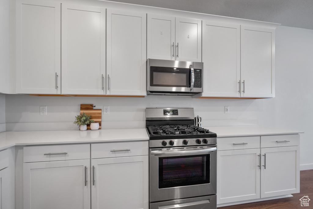 Kitchen featuring appliances with stainless steel finishes, white cabinetry, light countertops, and dark wood-type flooring