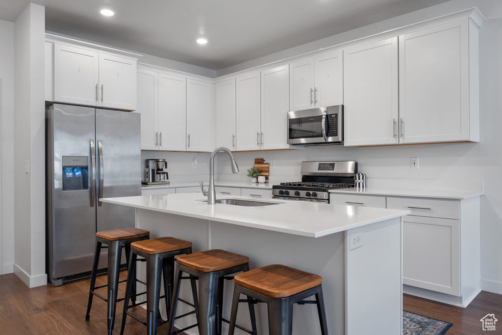 Kitchen with appliances with stainless steel finishes, dark wood-style flooring, a breakfast bar area, white cabinets, and recessed lighting
