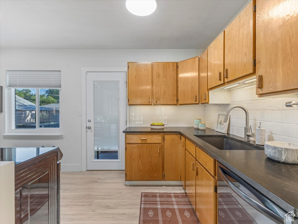 Kitchen featuring dishwasher, dark countertops, backsplash, and light wood-style floors