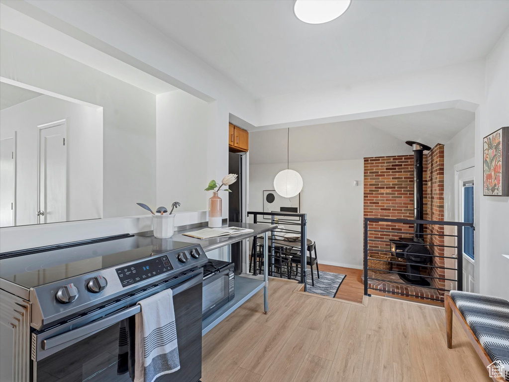 Kitchen with stainless steel range with electric stovetop, light wood-style flooring, a wood stove, lofted ceiling, and hanging light fixtures