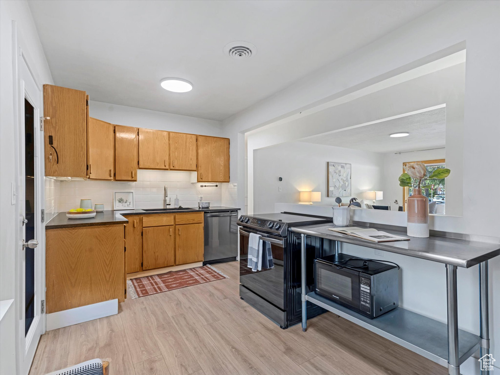 Kitchen featuring black appliances, light wood finished floors, decorative backsplash, dark countertops, and brown cabinets