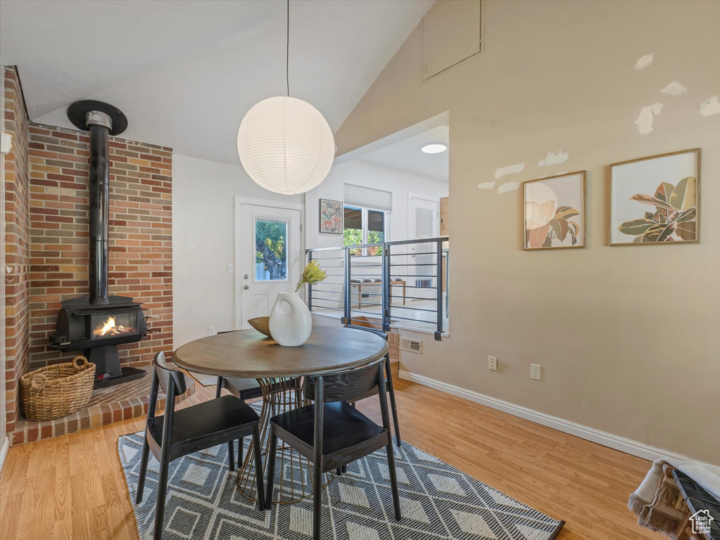 Dining area with a wood stove, light wood-style flooring, and lofted ceiling