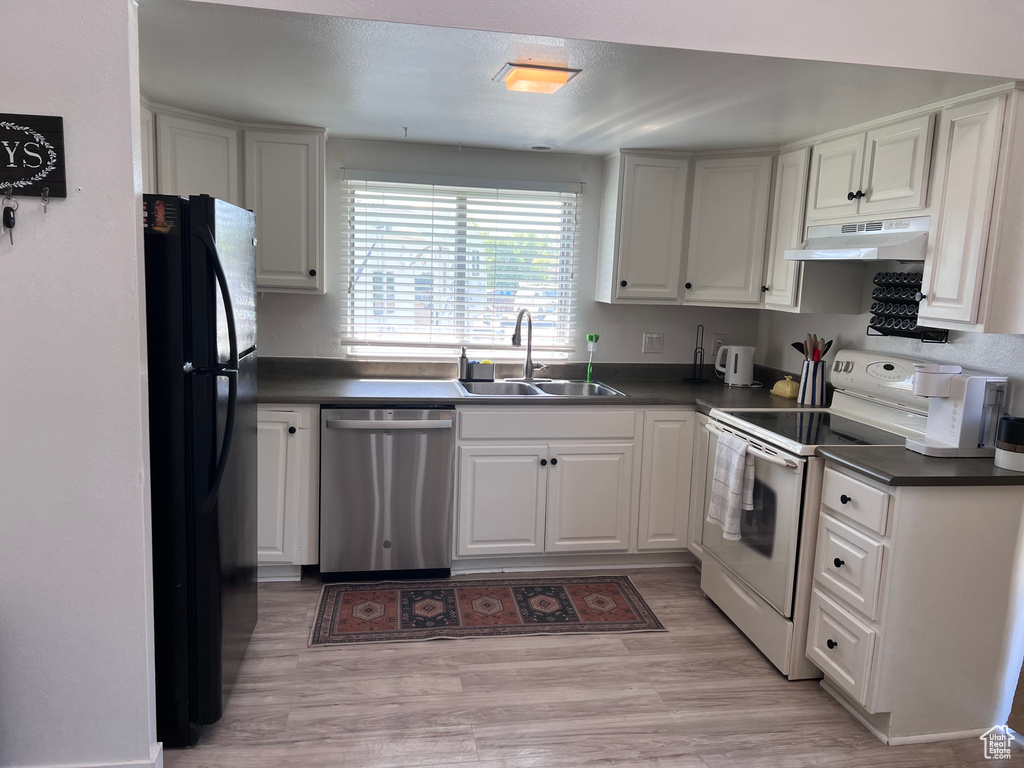 Kitchen with dishwasher, white range with electric stovetop, freestanding refrigerator, under cabinet range hood, and dark countertops
