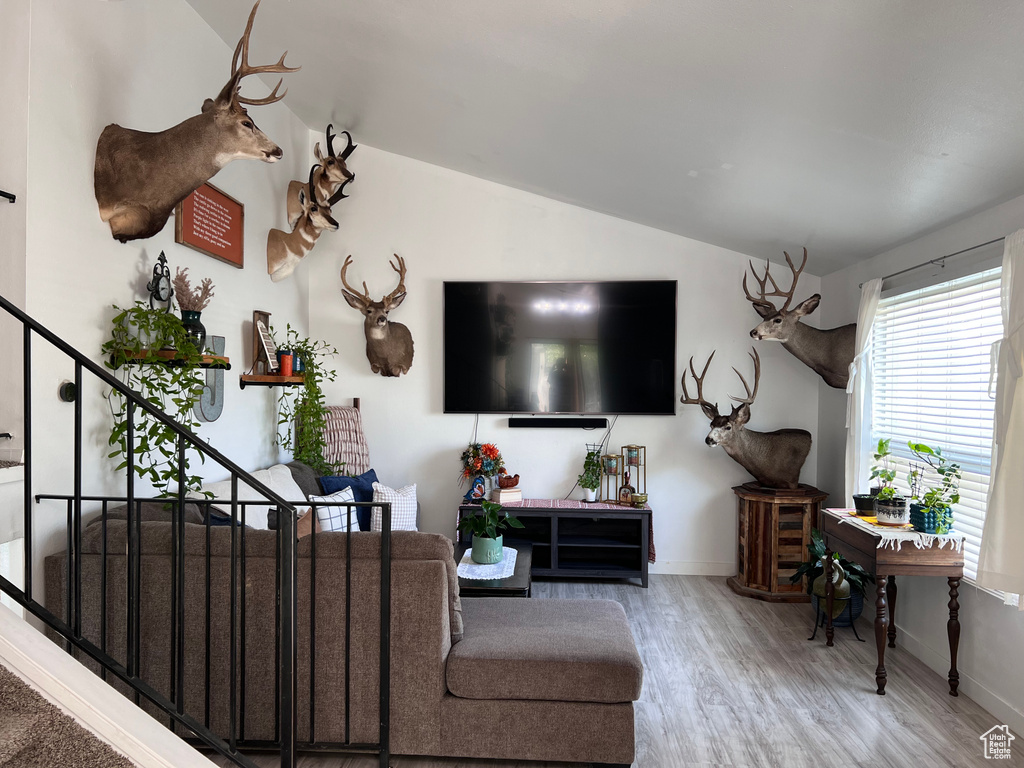 Living area with vaulted ceiling, wood finished floors, and stairs