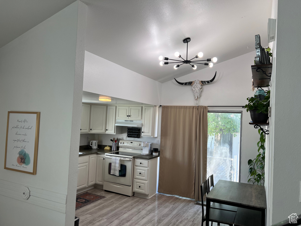 Kitchen with white electric stove, under cabinet range hood, a chandelier, dark countertops, and light wood finished floors