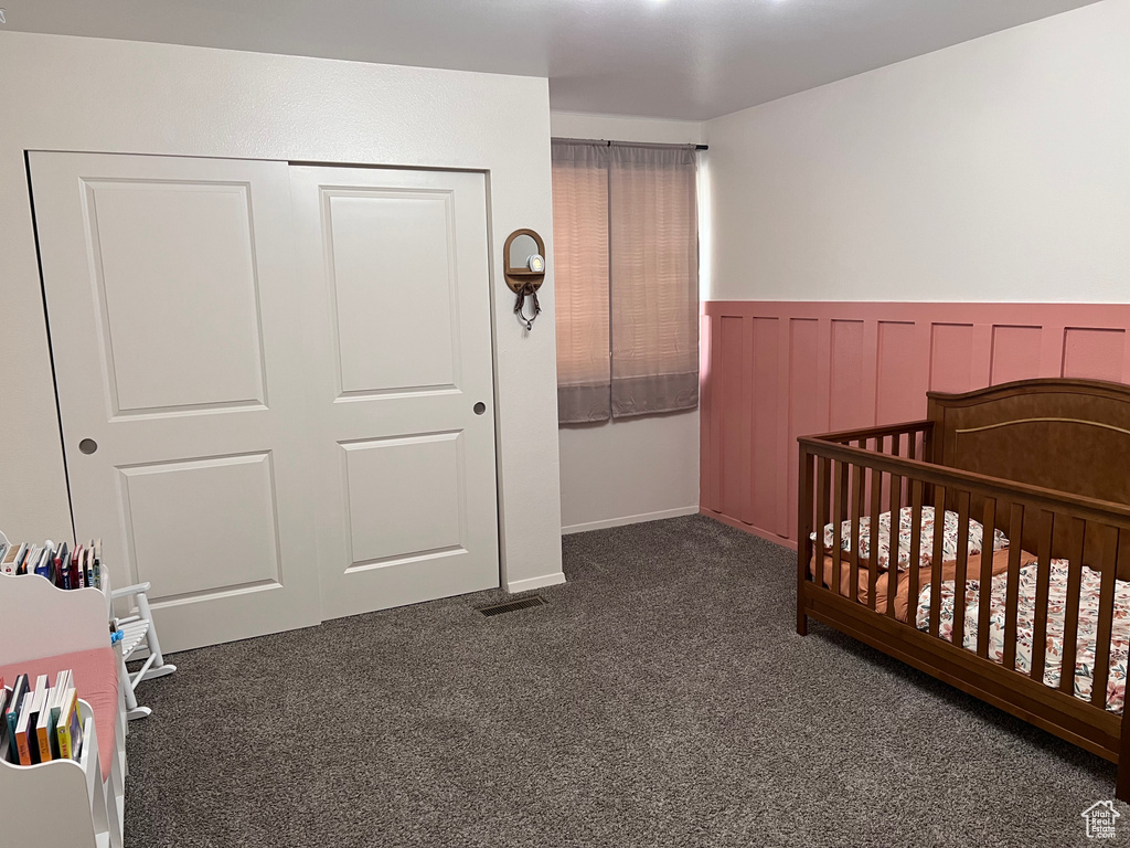 Carpeted bedroom with a nursery area, a wainscoted wall, and a closet
