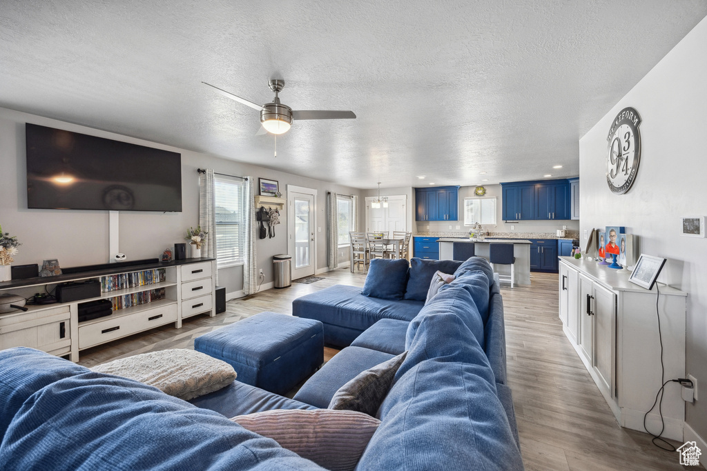 Living room with a textured ceiling, ceiling fan, and light wood finished floors