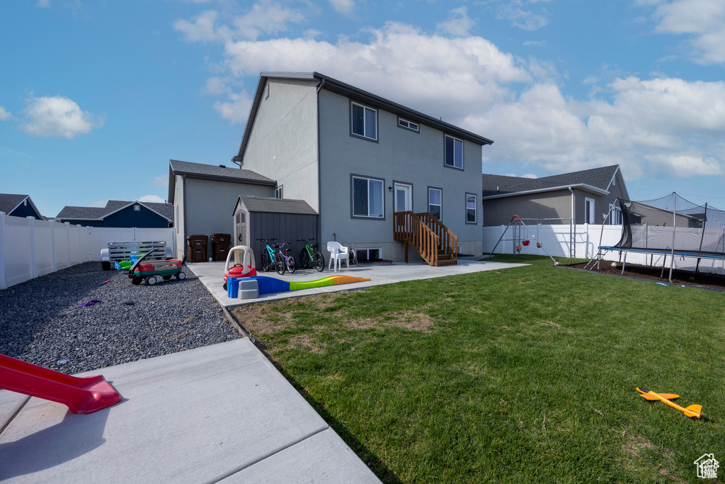 Back of property featuring a trampoline, a storage unit, a patio, a fenced backyard, and stucco siding