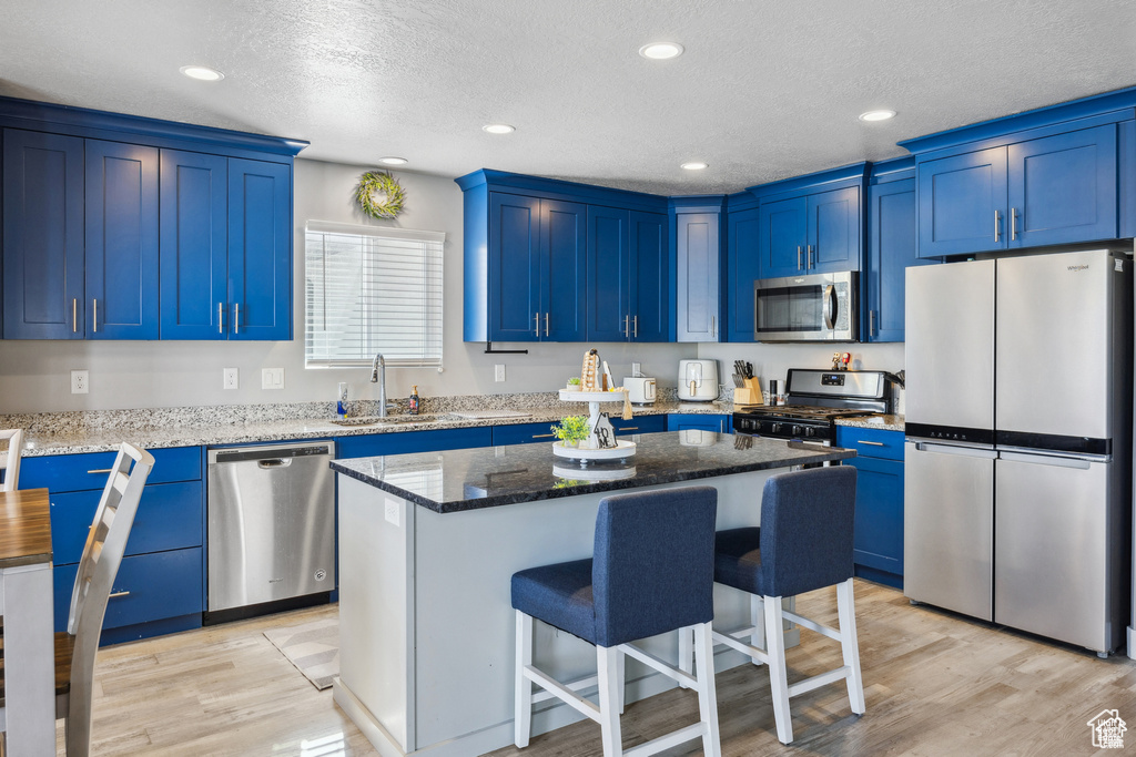 Kitchen featuring stainless steel appliances, blue cabinets, a kitchen breakfast bar, recessed lighting, and a textured ceiling