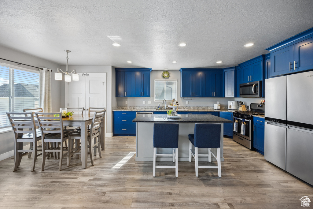 Kitchen with stainless steel appliances, blue cabinetry, a kitchen island, a breakfast bar area, and recessed lighting