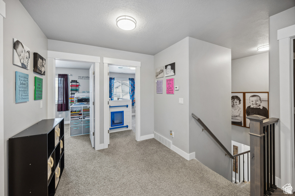 Hall with an upstairs landing, a textured ceiling, and carpet floors