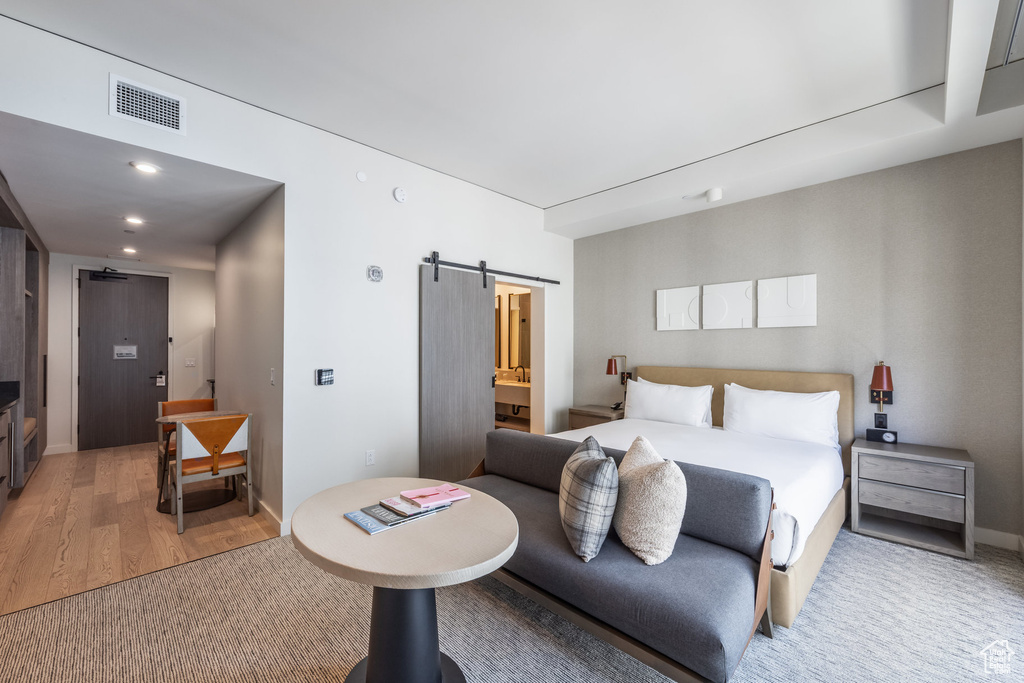 Bedroom with light wood-style floors, a barn door, recessed lighting, and ensuite bath