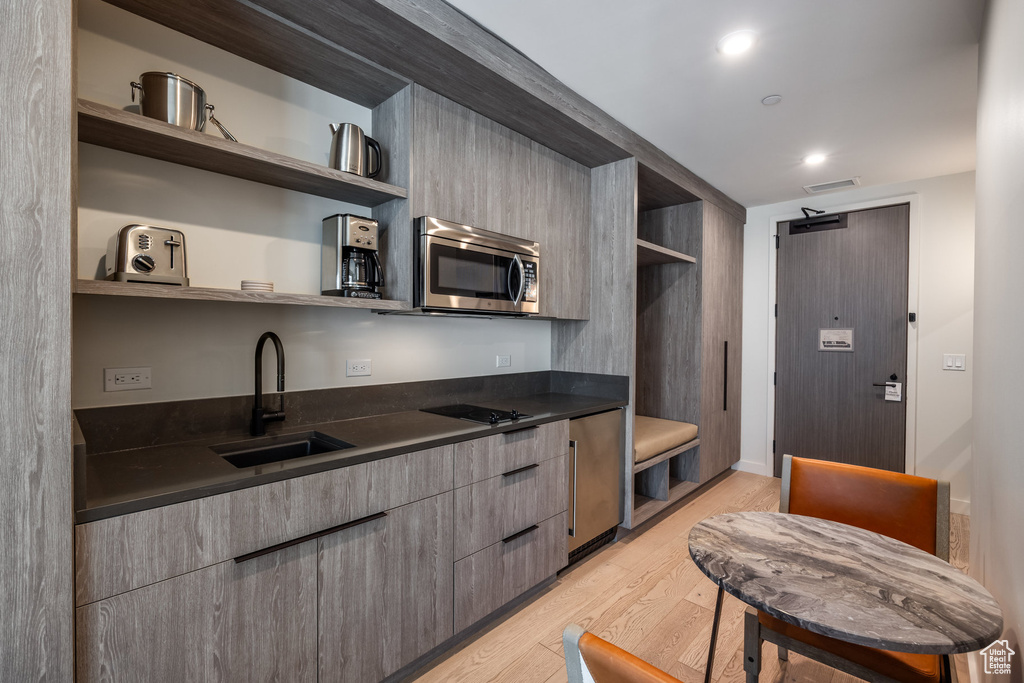 Kitchen with open shelves, stainless steel microwave, dark countertops, light wood finished floors, and recessed lighting