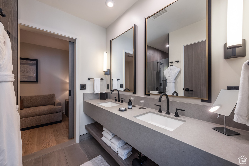 Bathroom with double vanity, wood finished floors, tiled shower, and recessed lighting